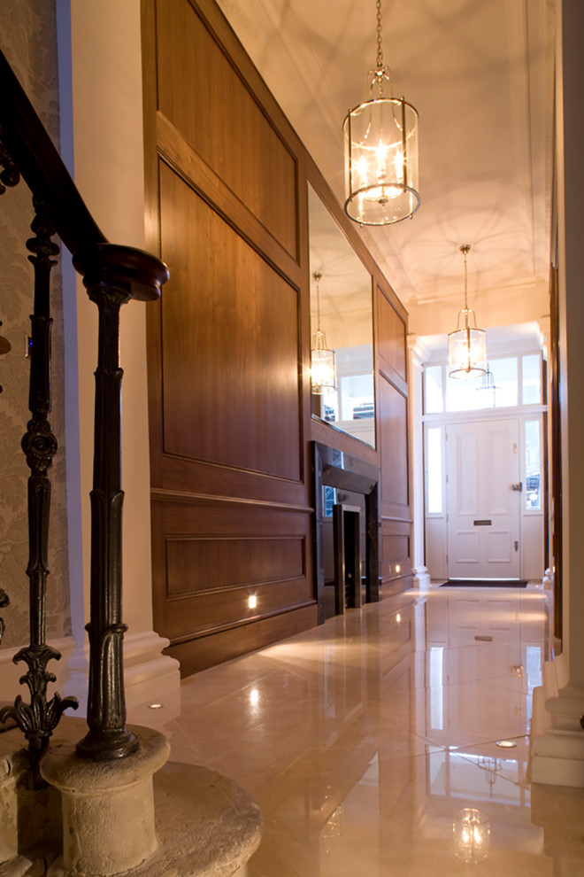 Cette image montre une grande entrée bohème avec un couloir, un mur marron, un sol en marbre, une porte simple, une porte blanche, un sol beige et du lambris.