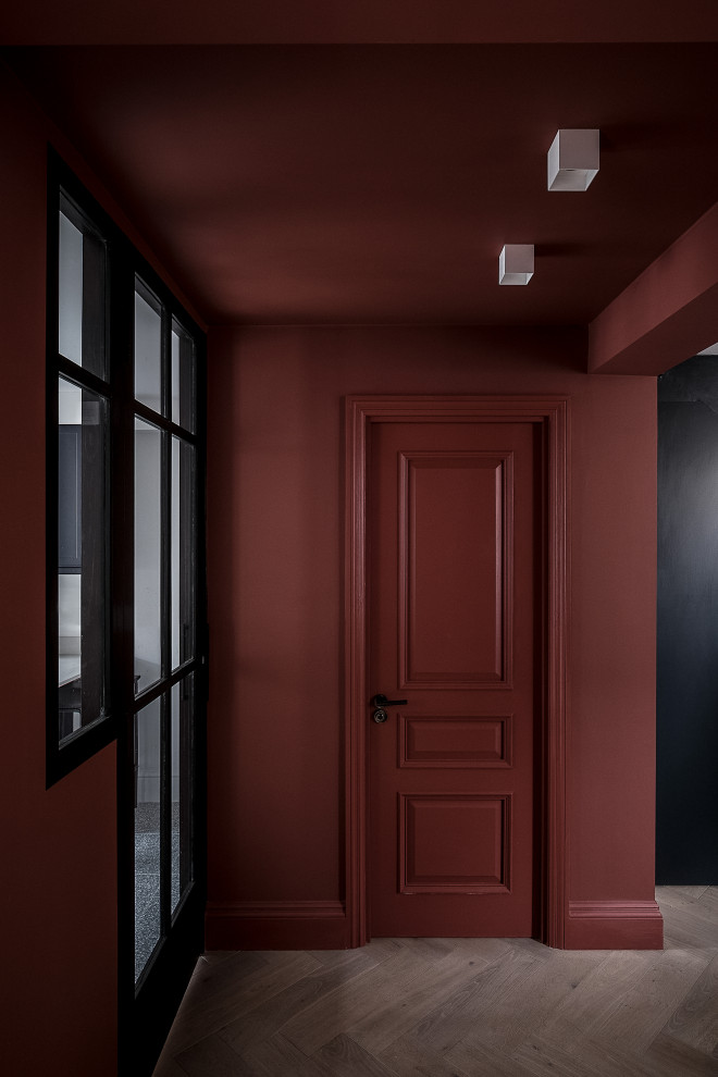 Esempio di un corridoio minimal di medie dimensioni con pareti rosse, pavimento in legno massello medio, una porta singola e una porta nera