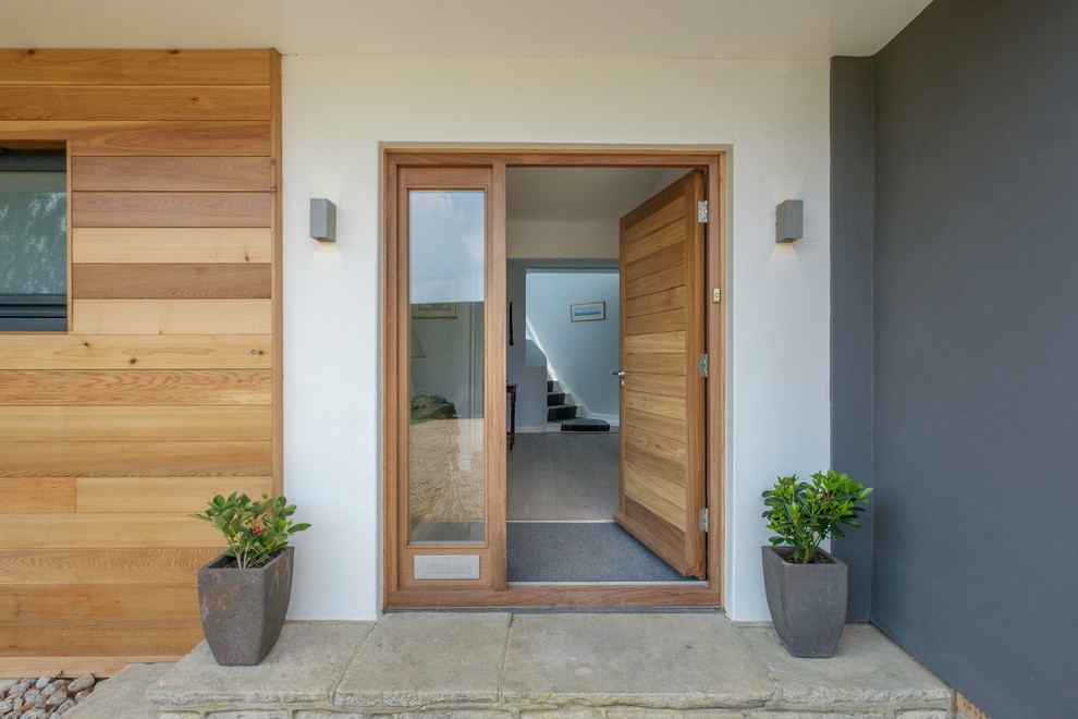 На фото: входная дверь в современном стиле с белыми стенами, одностворчатой входной дверью, входной дверью из дерева среднего тона и серым полом