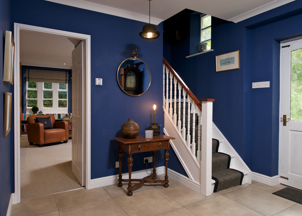 На фото: узкая прихожая в викторианском стиле с синими стенами, полом из керамогранита, одностворчатой входной дверью и белой входной дверью с