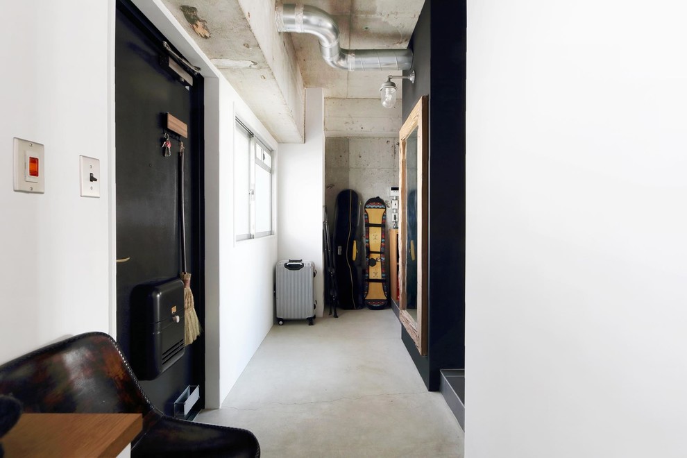 Bild på en industriell entré, med vita väggar, betonggolv, en enkeldörr, en svart dörr och grått golv