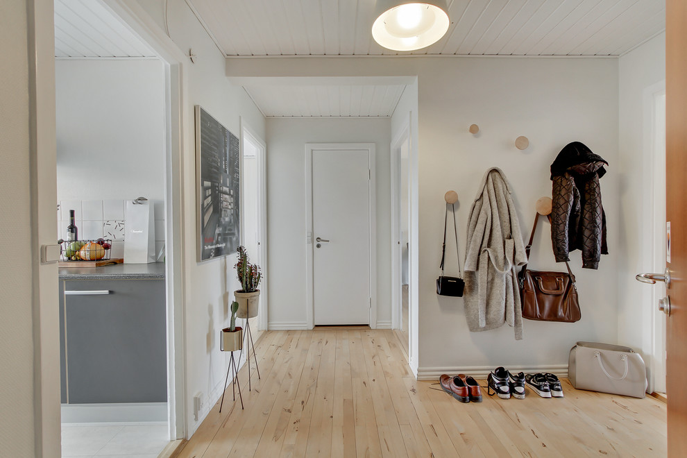 На фото: входная дверь среднего размера в скандинавском стиле с белыми стенами, светлым паркетным полом, одностворчатой входной дверью и белой входной дверью с