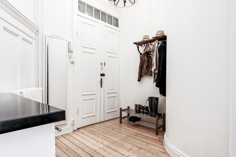 Inredning av ett minimalistiskt mellanstort kapprum, med vita väggar, ljust trägolv, en dubbeldörr och en vit dörr