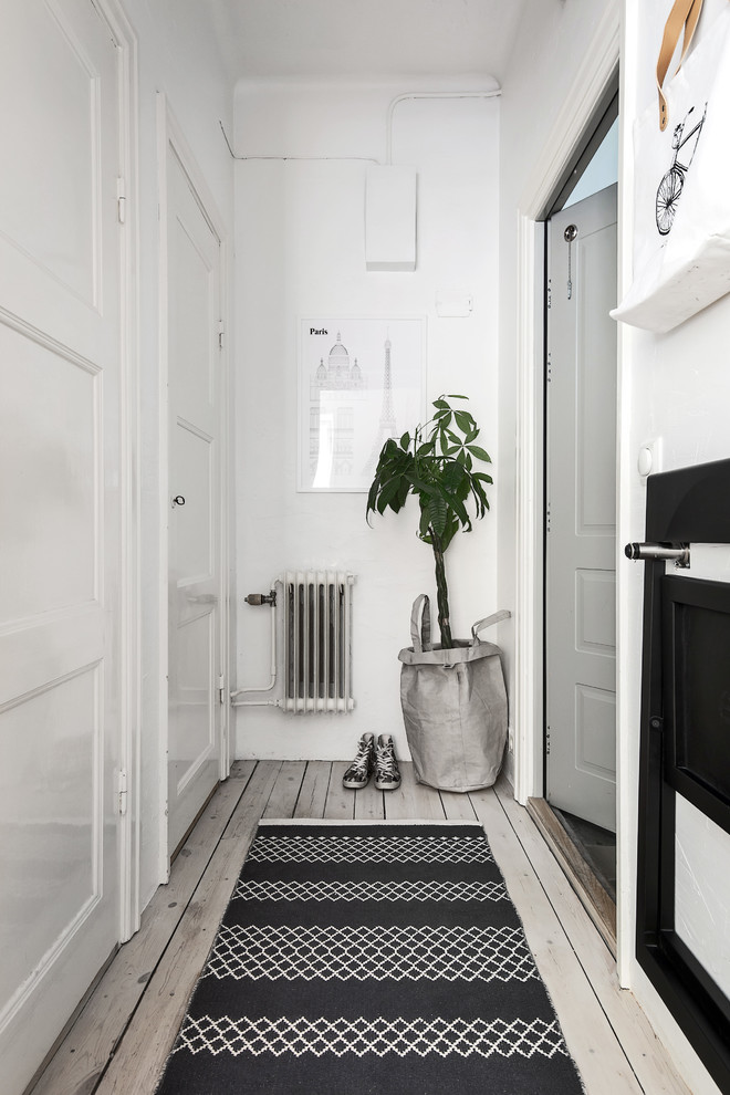 Идея дизайна: узкая прихожая в скандинавском стиле с белыми стенами, светлым паркетным полом, одностворчатой входной дверью и серой входной дверью