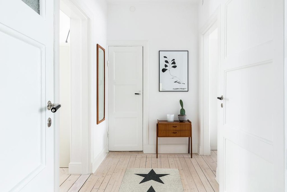 Diseño de hall escandinavo grande con suelo de madera clara, puerta simple, puerta blanca y paredes blancas