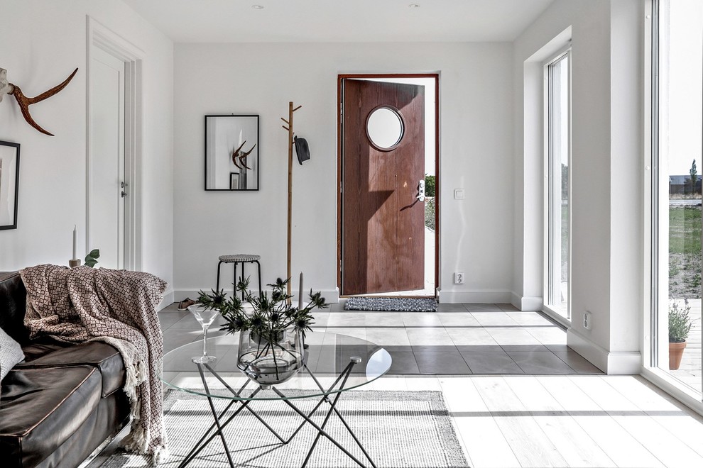 На фото: узкая прихожая среднего размера в скандинавском стиле с белыми стенами, полом из керамической плитки, одностворчатой входной дверью, коричневой входной дверью и серым полом