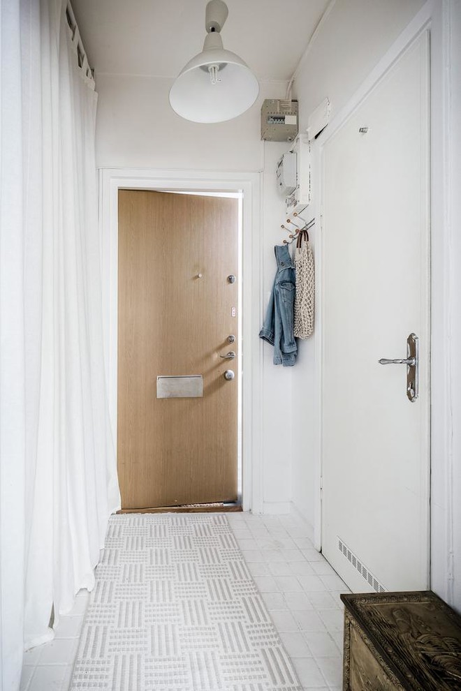 This is an example of a small scandi hallway in Stockholm with white walls, a single front door, a light wood front door and white floors.