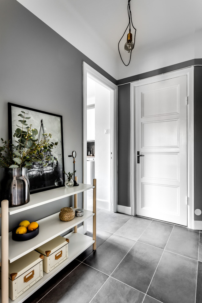 Scandinavian hallway in Stockholm with grey walls, a single front door, a white front door and grey floors.