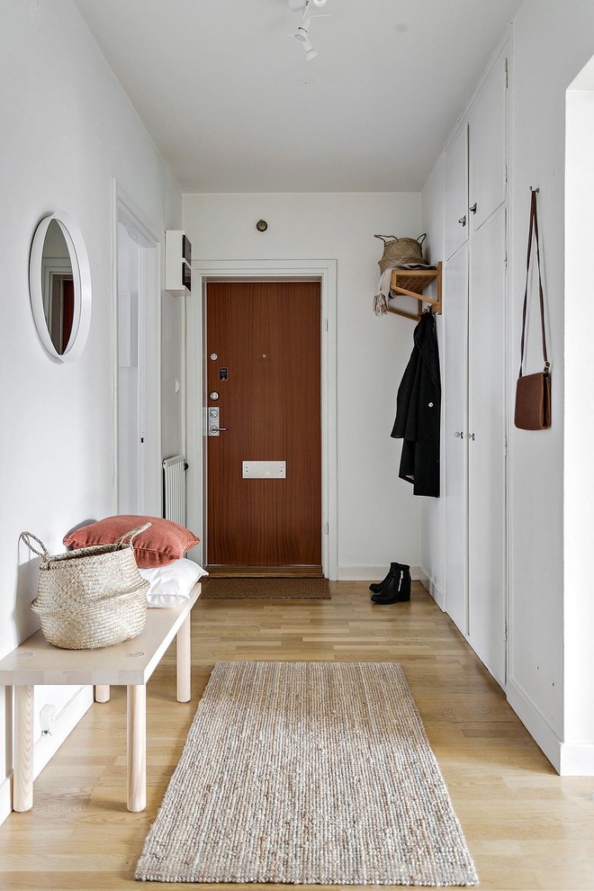 Стильный дизайн: узкая прихожая в скандинавском стиле с белыми стенами, светлым паркетным полом, одностворчатой входной дверью, входной дверью из дерева среднего тона и бежевым полом - последний тренд