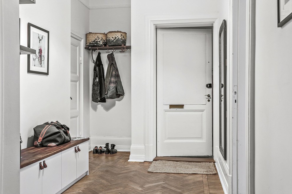 Cette image montre une entrée nordique de taille moyenne avec un couloir, un mur blanc, un sol en bois brun, une porte simple et une porte blanche.