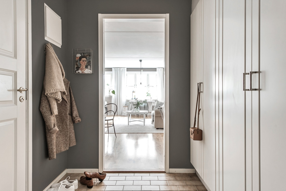Minimalistisk inredning av ett mellanstort kapprum, med grå väggar, tegelgolv, en enkeldörr, en vit dörr och brunt golv