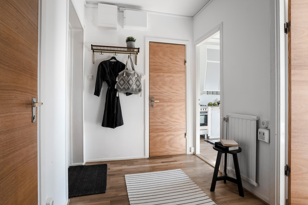Foto de hall nórdico de tamaño medio con paredes blancas, suelo de madera en tonos medios, puerta simple, puerta de madera en tonos medios y suelo marrón
