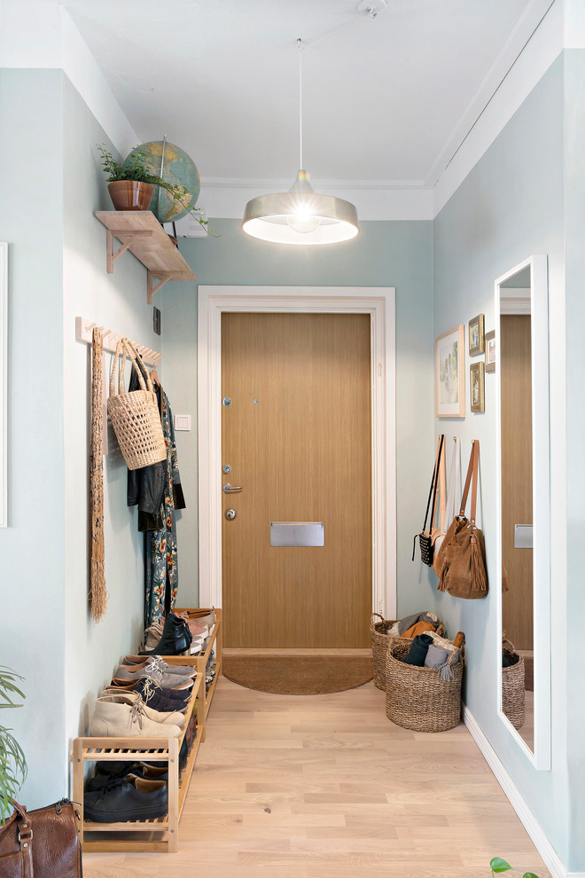 Foto på en minimalistisk entré, med blå väggar, ljust trägolv, mellanmörk trädörr och en enkeldörr