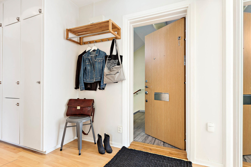 Modelo de puerta principal nórdica con paredes blancas, suelo de madera clara, puerta simple y puerta de madera clara