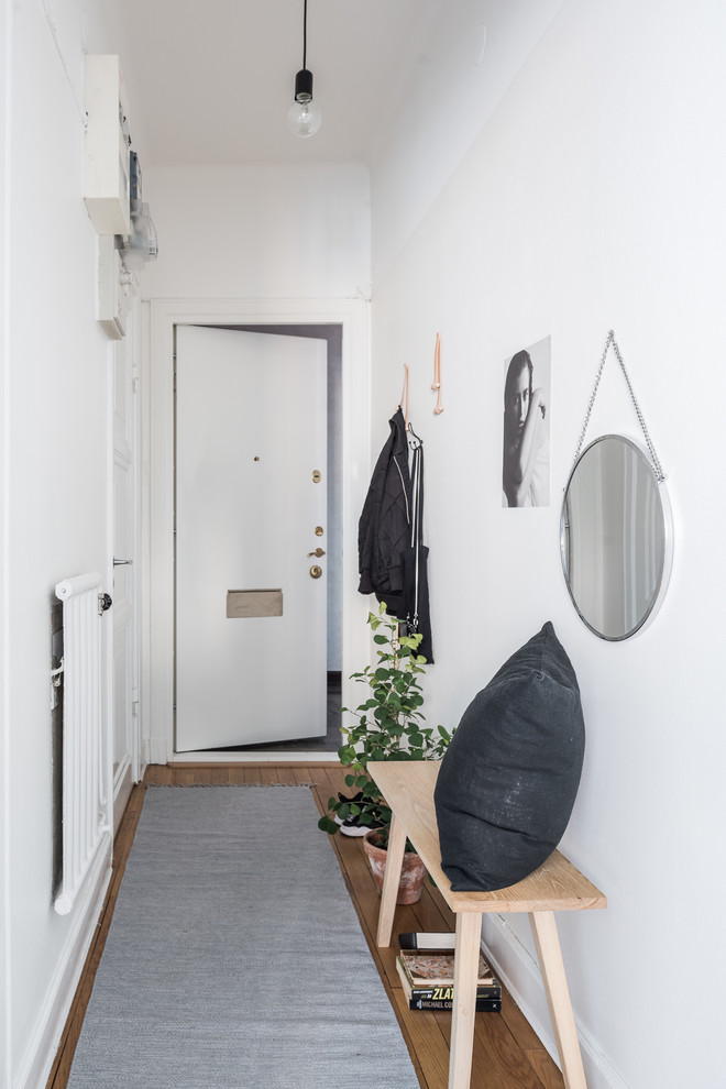 Идея дизайна: узкая прихожая среднего размера в скандинавском стиле с белыми стенами, светлым паркетным полом, одностворчатой входной дверью и белой входной дверью