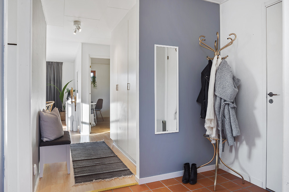 Пример оригинального дизайна: узкая прихожая в скандинавском стиле с фиолетовыми стенами, полом из терракотовой плитки, одностворчатой входной дверью, белой входной дверью и коричневым полом