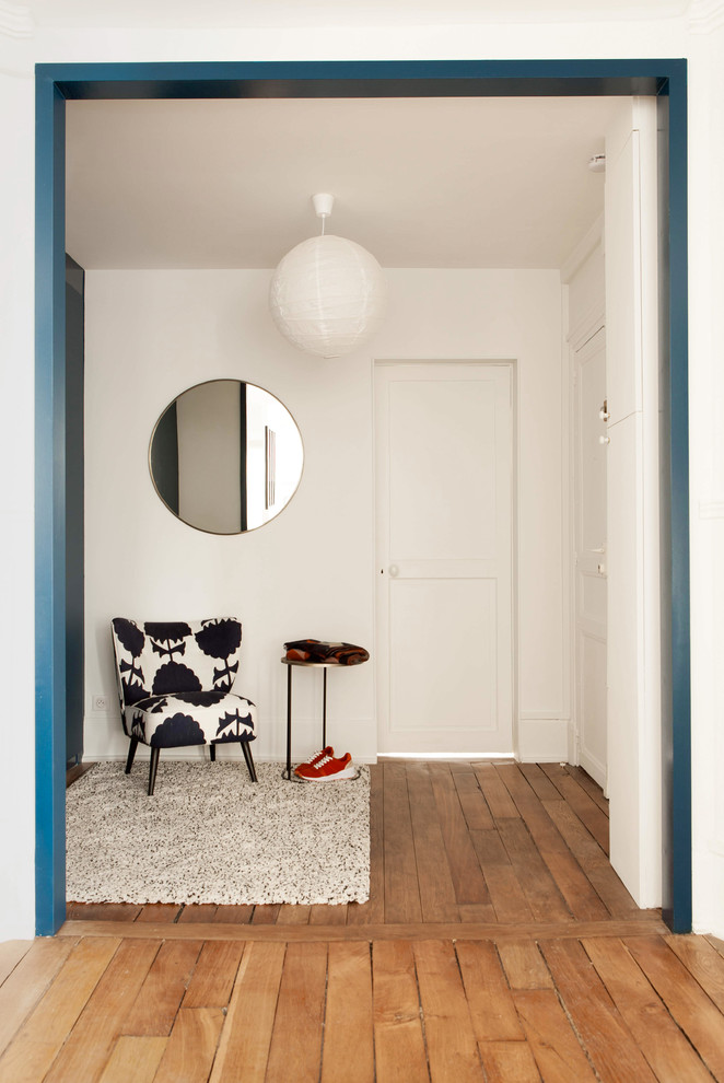 Réalisation d'une entrée design de taille moyenne avec un vestiaire, un mur blanc, un sol en bois brun et une porte blanche.