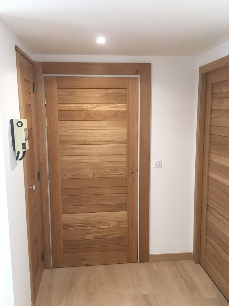This is an example of a medium sized contemporary foyer in Nice with white walls, light hardwood flooring and a medium wood front door.