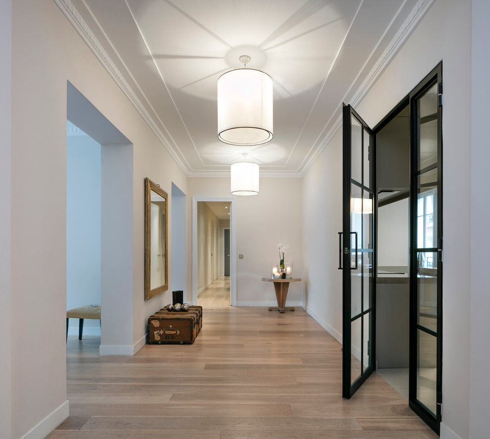 Cette image montre un grand hall d'entrée design avec un mur blanc et parquet clair.
