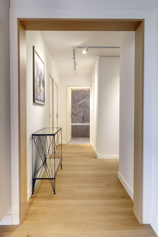 На фото: узкая прихожая среднего размера в стиле модернизм с белыми стенами, светлым паркетным полом, одностворчатой входной дверью, белой входной дверью, коричневым полом и обоями на стенах с