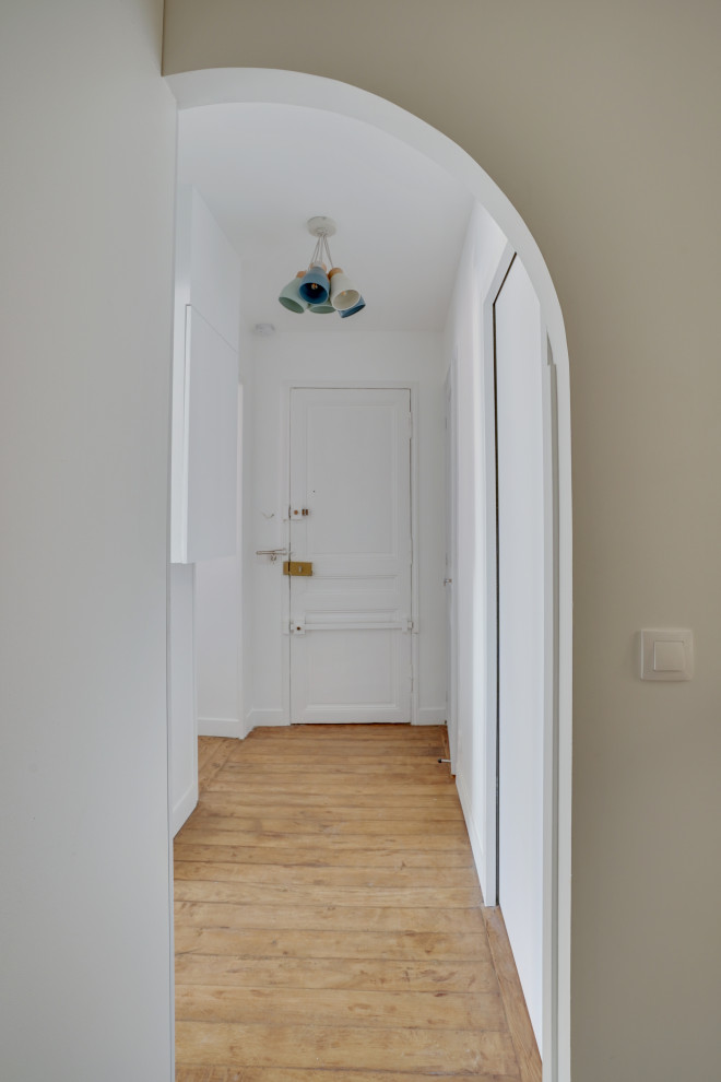 Cette photo montre un petit hall d'entrée moderne avec un mur blanc, parquet clair, une porte blanche et une porte simple.