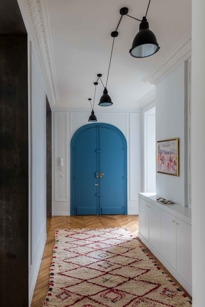 Modern inredning av en hall, med vita väggar, mellanmörkt trägolv, en dubbeldörr, en blå dörr och brunt golv