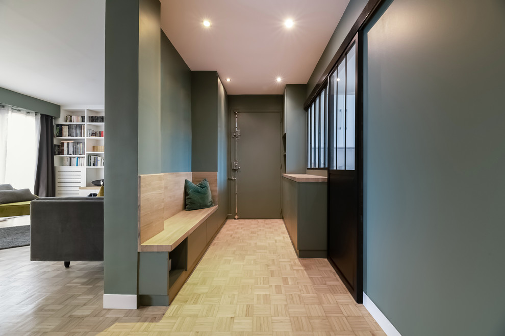 Cette image montre une entrée design de taille moyenne avec un couloir, un mur vert, parquet clair, une porte pivot, une porte verte et un sol beige.