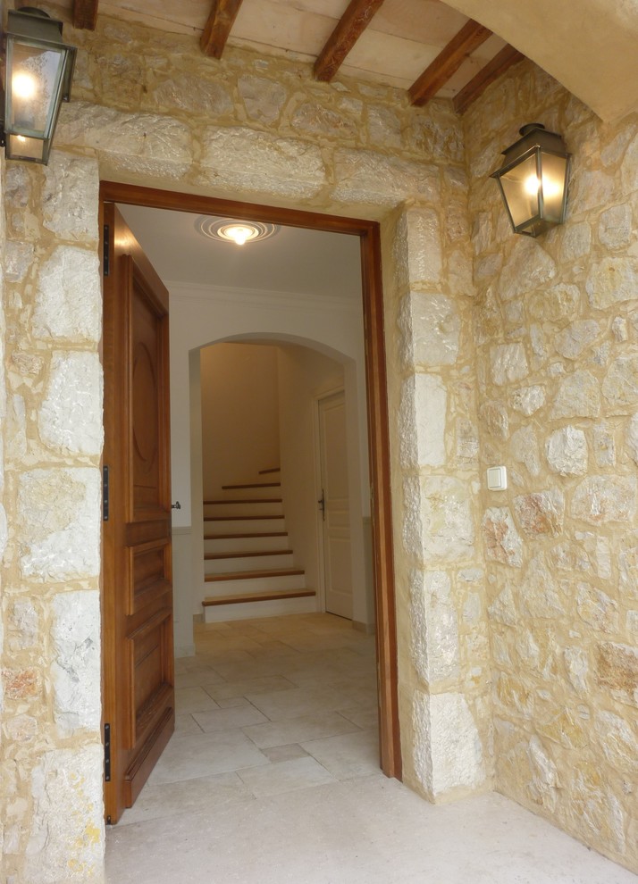 Aménagement d'un grand hall d'entrée méditerranéen avec un mur blanc, un sol en carrelage de céramique, une porte simple, une porte en bois brun et un sol beige.