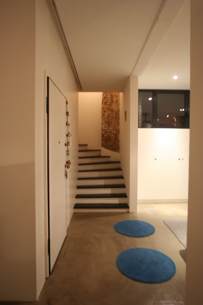 На фото: узкая прихожая среднего размера в современном стиле с белыми стенами, бетонным полом, одностворчатой входной дверью и белой входной дверью с