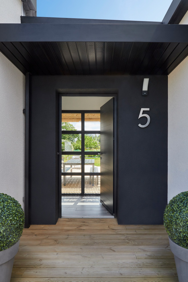 Exempel på en mellanstor modern ingång och ytterdörr, med svarta väggar, ljust trägolv, en enkeldörr, en svart dörr och brunt golv