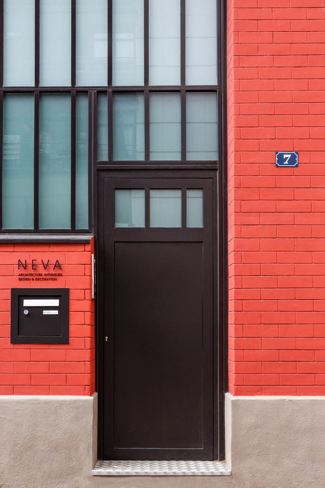 Inredning av en industriell mellanstor ingång och ytterdörr, med röda väggar, tegelgolv, en enkeldörr, en brun dörr och rött golv