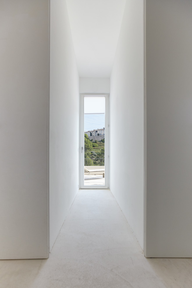 Réalisation d'une grande entrée minimaliste avec un couloir, un mur blanc, sol en béton ciré, une porte pivot, une porte en bois clair et un sol blanc.