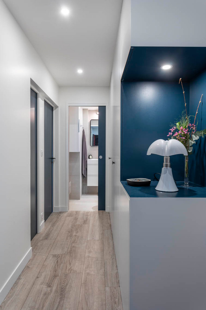Cette photo montre une entrée moderne de taille moyenne avec un couloir, un mur bleu, parquet clair, une porte blanche et un sol gris.