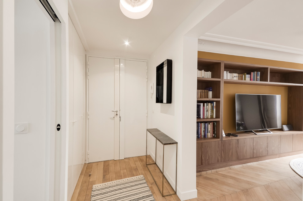 Cette image montre une entrée design de taille moyenne avec un couloir, un mur blanc, parquet clair, une porte simple, une porte blanche et un sol marron.