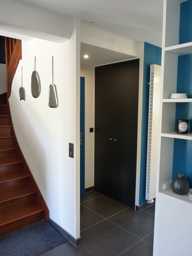 Aménagement d'un hall d'entrée contemporain de taille moyenne avec un mur bleu, un sol en carrelage de céramique, un sol noir et une porte blanche.