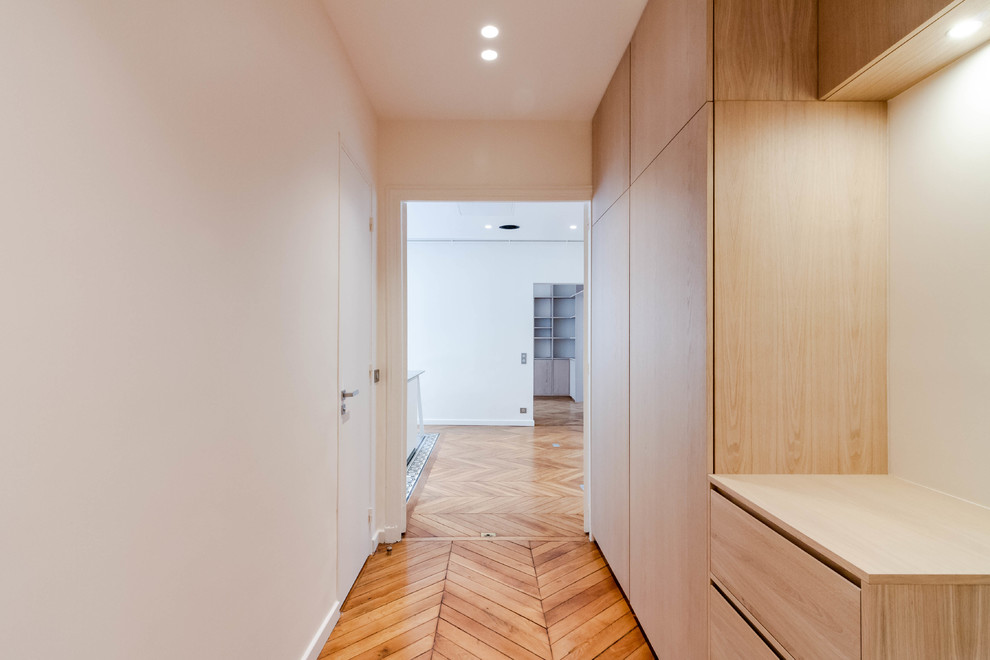 Cette image montre une entrée minimaliste de taille moyenne avec un couloir, un mur rose, un sol en bois brun, une porte double et un sol marron.