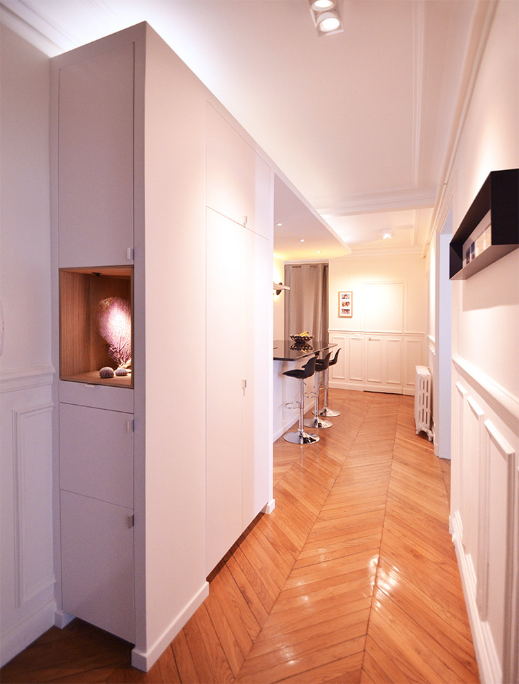 На фото: узкая прихожая среднего размера в современном стиле с белыми стенами, паркетным полом среднего тона, поворотной входной дверью, белой входной дверью и коричневым полом