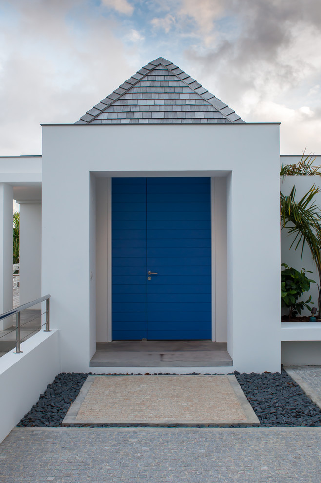 Bild på en stor tropisk ingång och ytterdörr, med vita väggar, betonggolv, en enkeldörr och en blå dörr