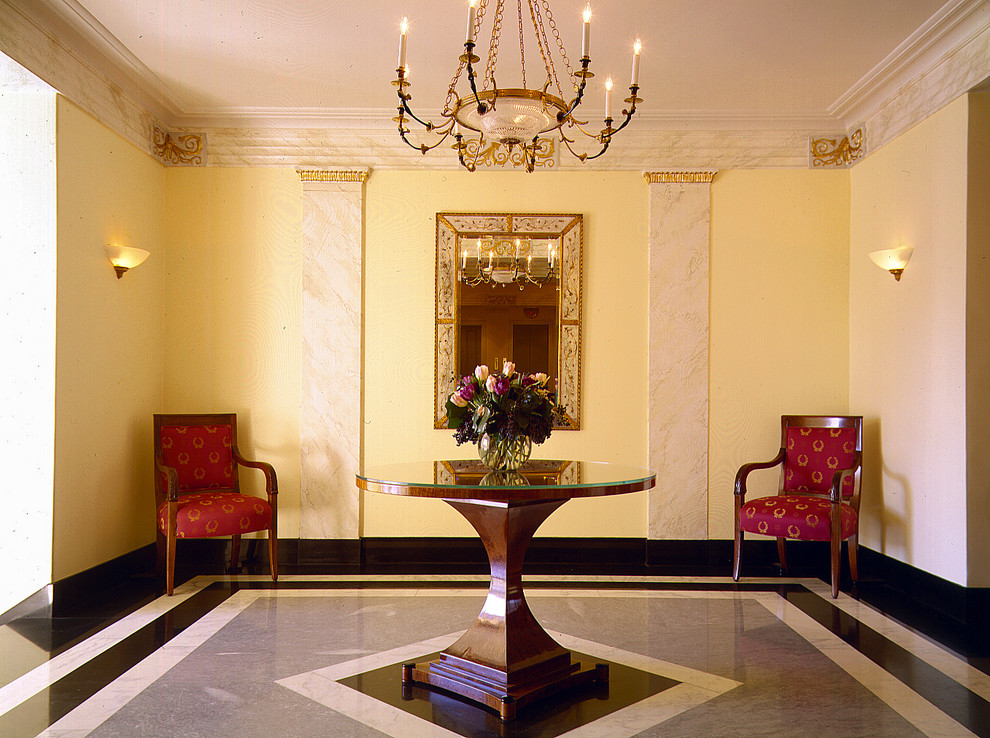 Cette image montre un grand hall d'entrée traditionnel avec un mur jaune, un sol en marbre et un sol multicolore.