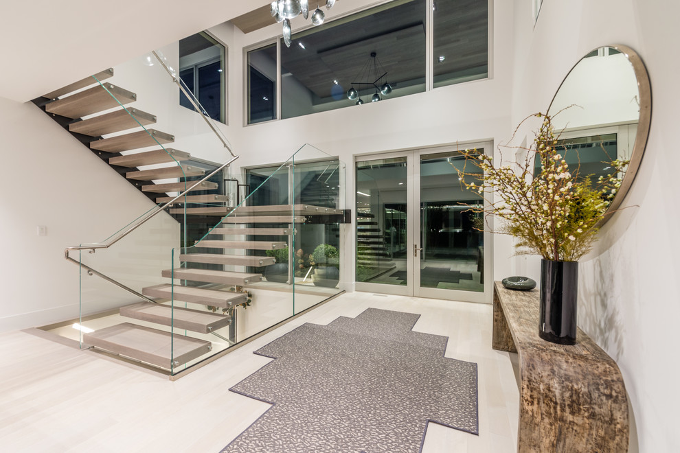This is an example of an expansive contemporary foyer in New York with white walls, light hardwood flooring, a pivot front door, a glass front door and beige floors.