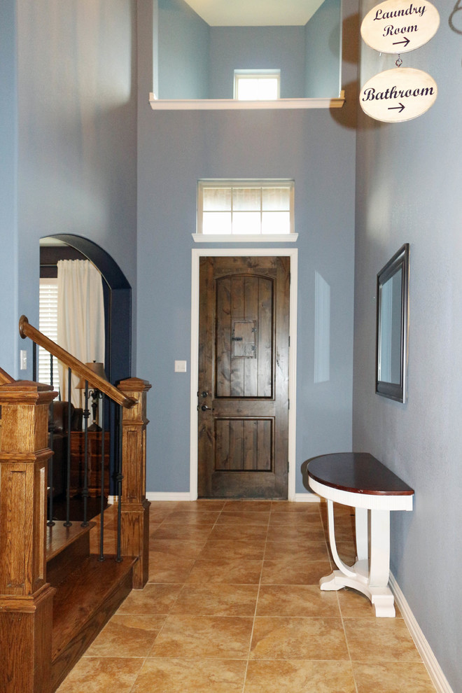 Réalisation d'un grand hall d'entrée tradition avec un mur bleu, un sol en carrelage de céramique, une porte simple, une porte en bois foncé et un sol beige.