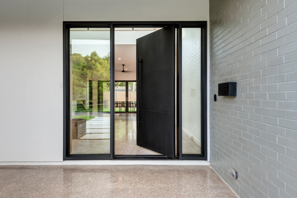 Idée de décoration pour une porte d'entrée minimaliste avec un mur gris, sol en béton ciré, une porte pivot, une porte noire, un mur en parement de brique et un sol gris.