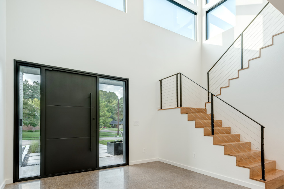 Пример оригинального дизайна: входная дверь в стиле модернизм с серыми стенами, бетонным полом, поворотной входной дверью, черной входной дверью, серым полом и кирпичными стенами