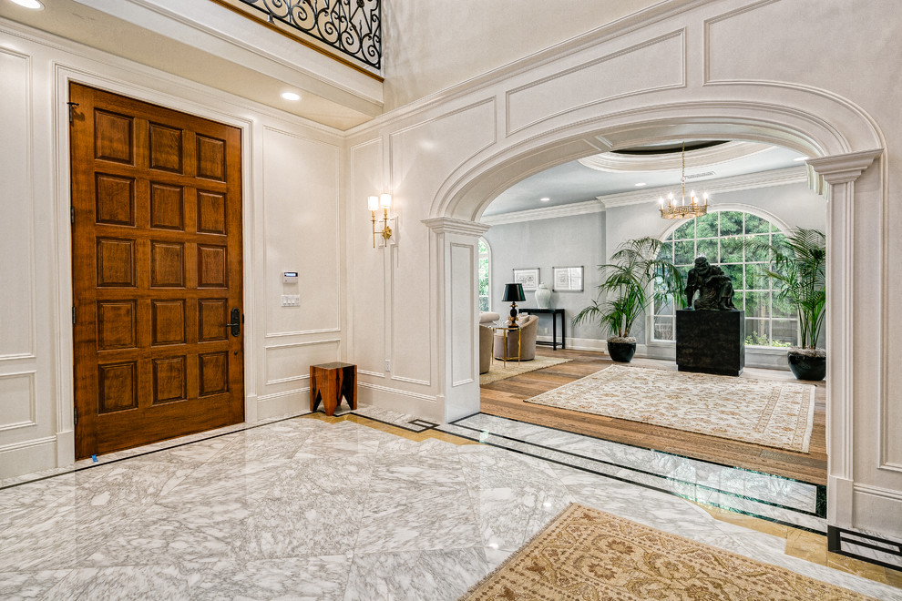 Klassisches Foyer mit weißer Wandfarbe, Marmorboden, Einzeltür, hellbrauner Holzhaustür und buntem Boden in Los Angeles