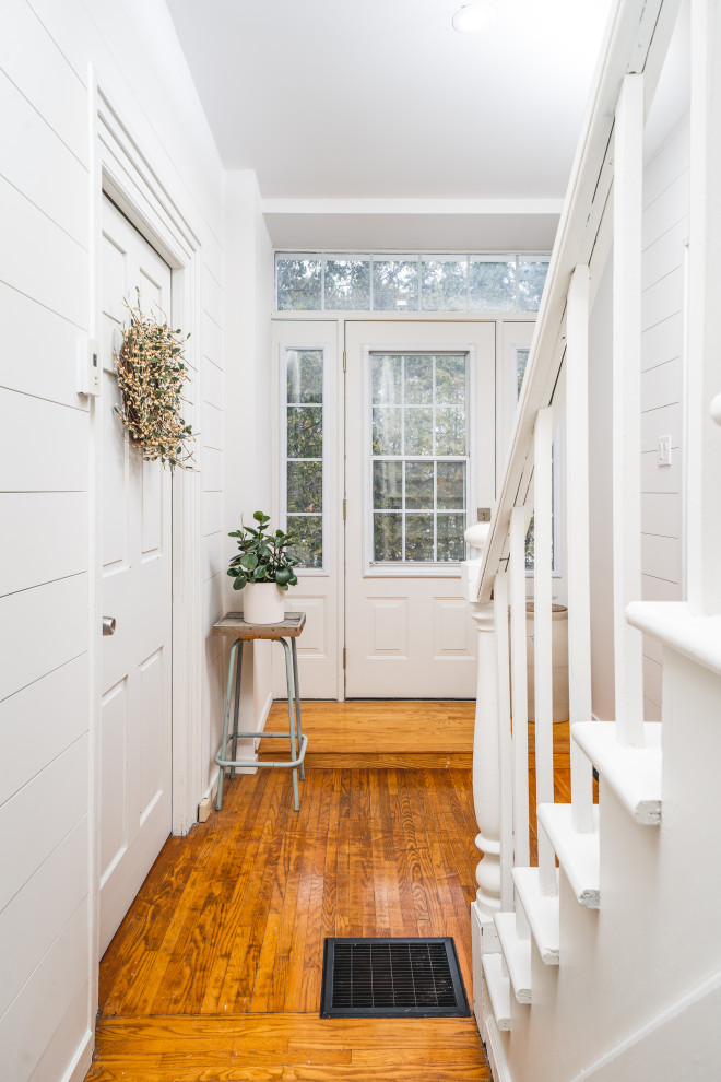 Esempio di un corridoio country di medie dimensioni con pareti bianche, pavimento in legno massello medio, una porta singola, una porta bianca e pavimento marrone