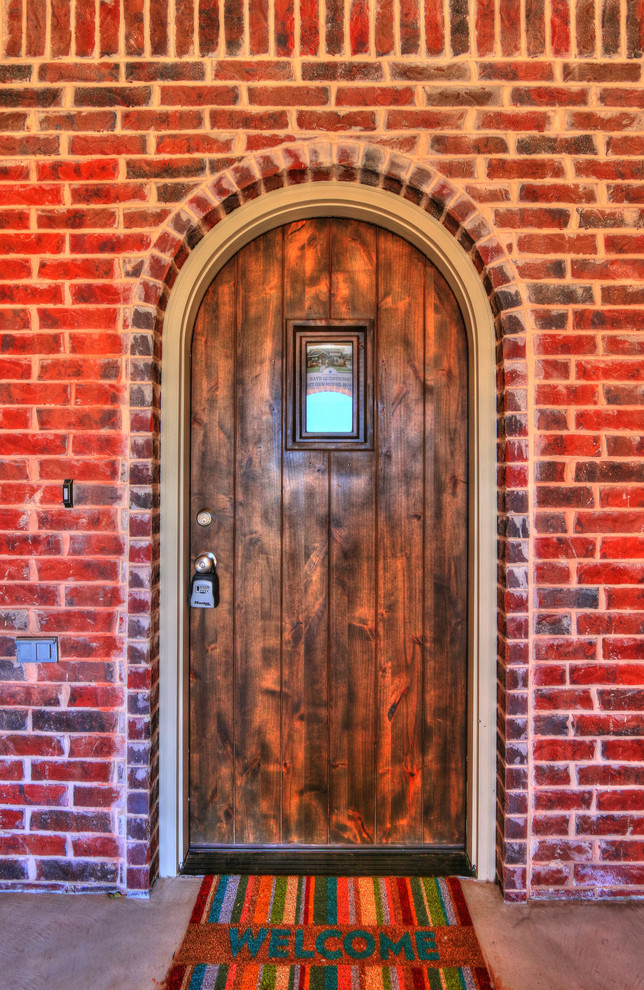 オクラホマシティにある高級な中くらいなサンタフェスタイルのおしゃれな玄関ドア (赤い壁、コンクリートの床、木目調のドア、グレーの床) の写真