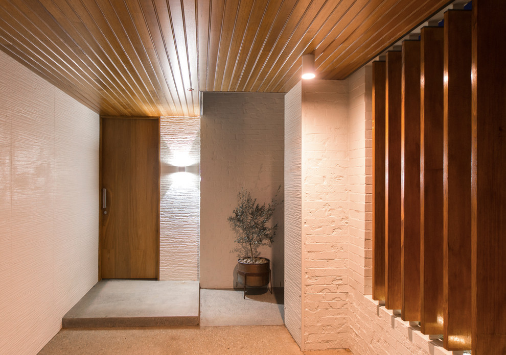 Diseño de puerta principal actual de tamaño medio con paredes blancas, suelo de cemento, puerta de madera oscura y suelo gris