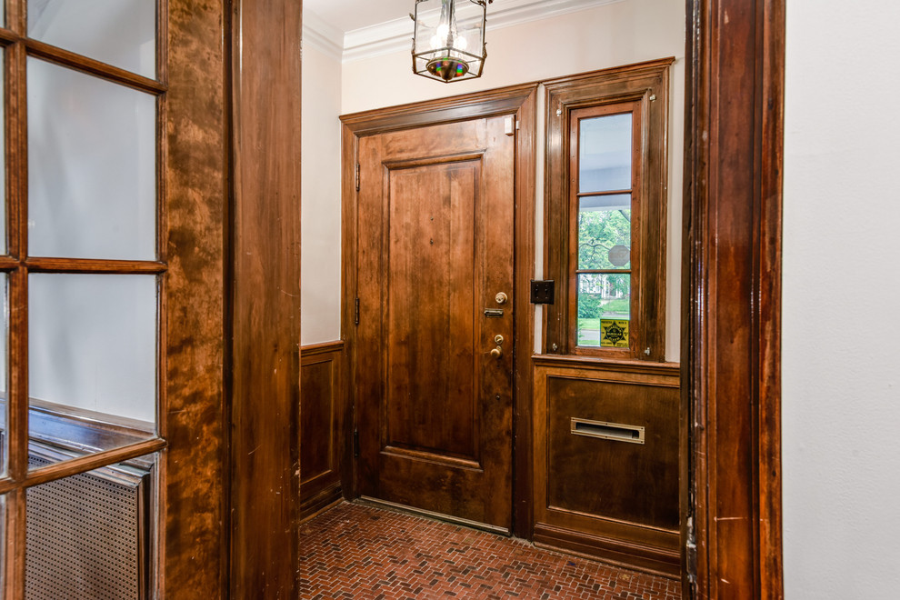 На фото: фойе среднего размера в классическом стиле с белыми стенами, одностворчатой входной дверью, входной дверью из дерева среднего тона и красным полом с