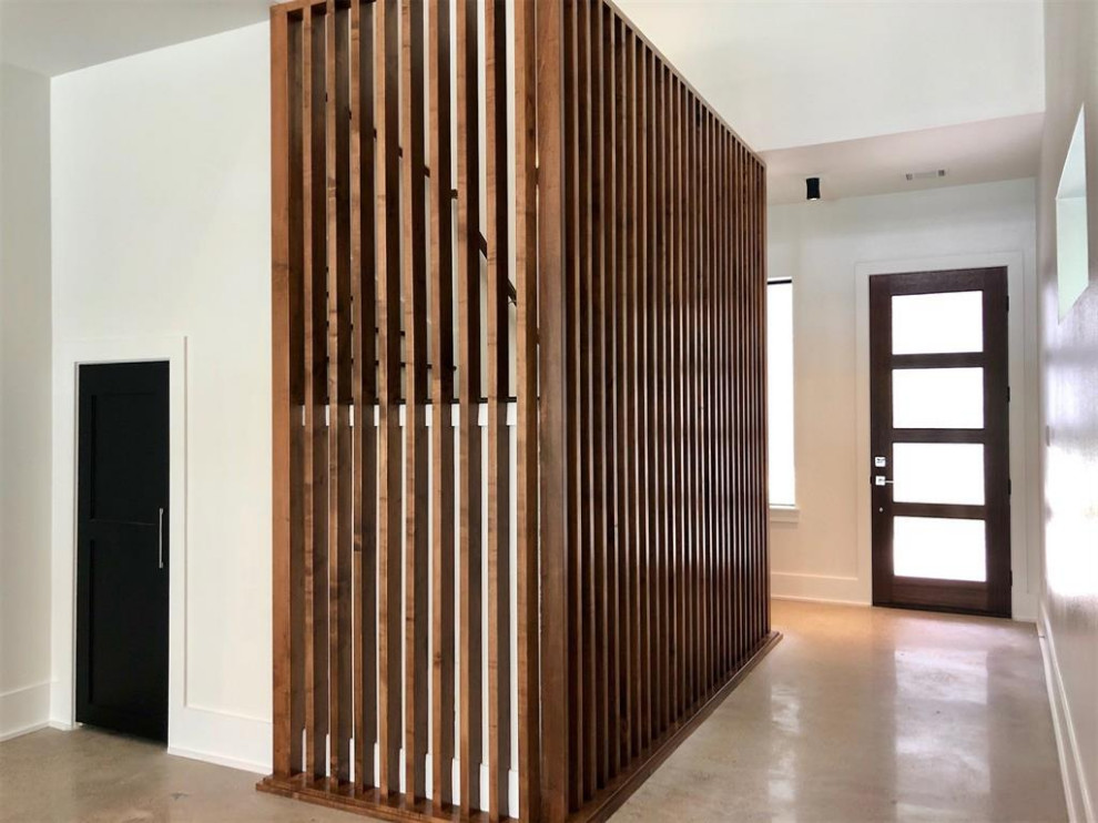 Cette image montre un grand hall d'entrée design avec sol en béton ciré, une porte simple, une porte en bois foncé et un sol gris.