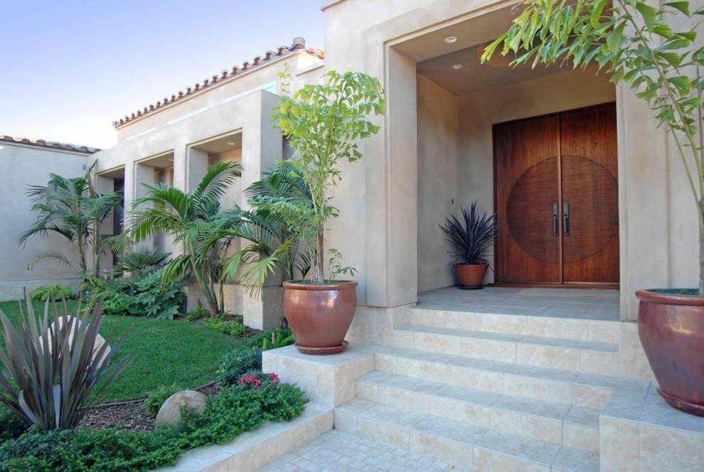 На фото: большая входная дверь в средиземноморском стиле с двустворчатой входной дверью, входной дверью из темного дерева, бежевыми стенами, полом из известняка и коричневым полом с